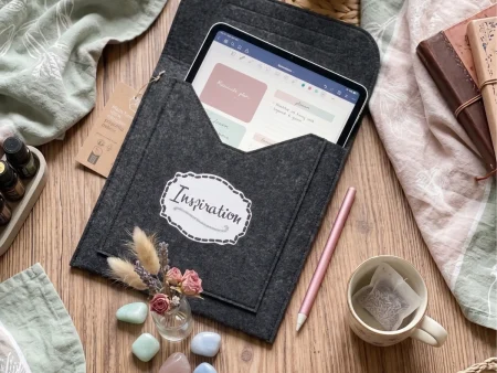 Housse de tablette en feutrine grise avec motif Inspiration posée sur un bureau en bois clair avec une tablette à moitié insérée.