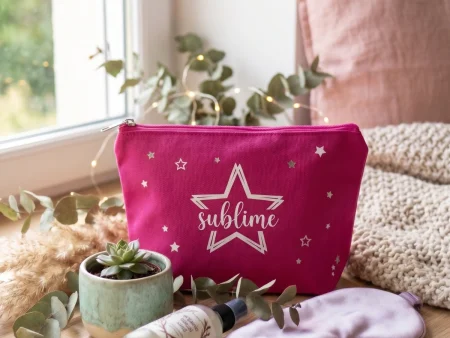 Pochette en coton fuchsia avec motif étoile et texte Sublime sur un rebord de fenêtre en bois avec un succulent et un masque de nuit.